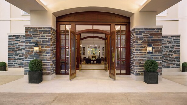 L’entrée d’un hôtel, avec une façade en pierre, de grandes portes en bois et une vue sur l’intérieur.