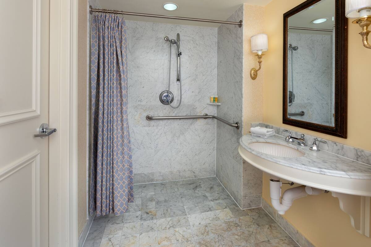 A bathroom with a shower, grab bars, a sink, and a mirror.
