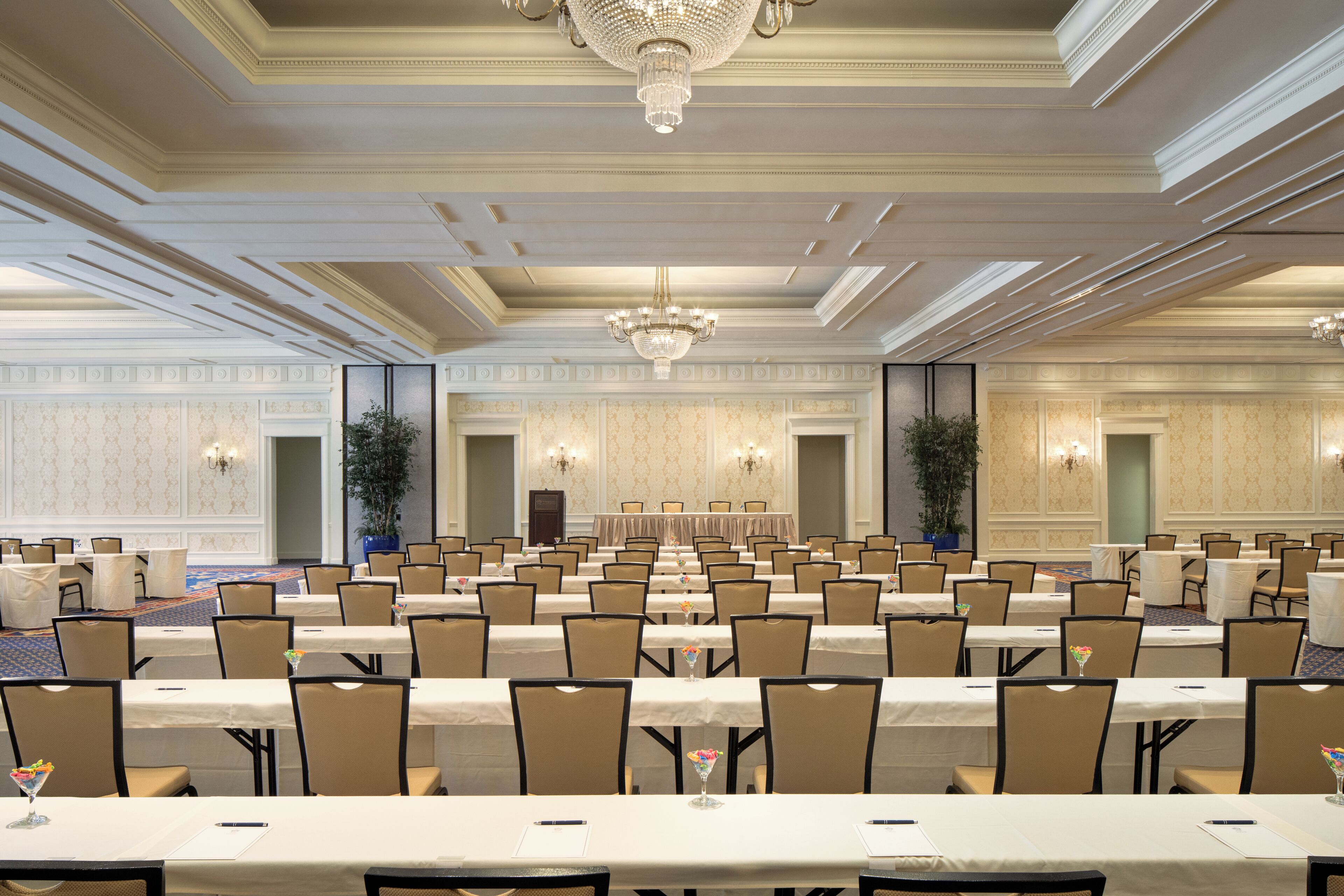Une vaste salle de banquet avec de longues rangées de tables et de chaises, des lustres et une scène.