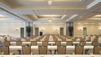 Une vaste salle de banquet avec de longues rangées de tables et de chaises, des lustres et une scène.
