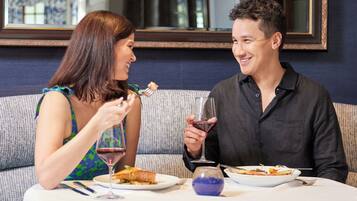A dining table with a white tablecloth, two plates of food, and a glass of red wine.