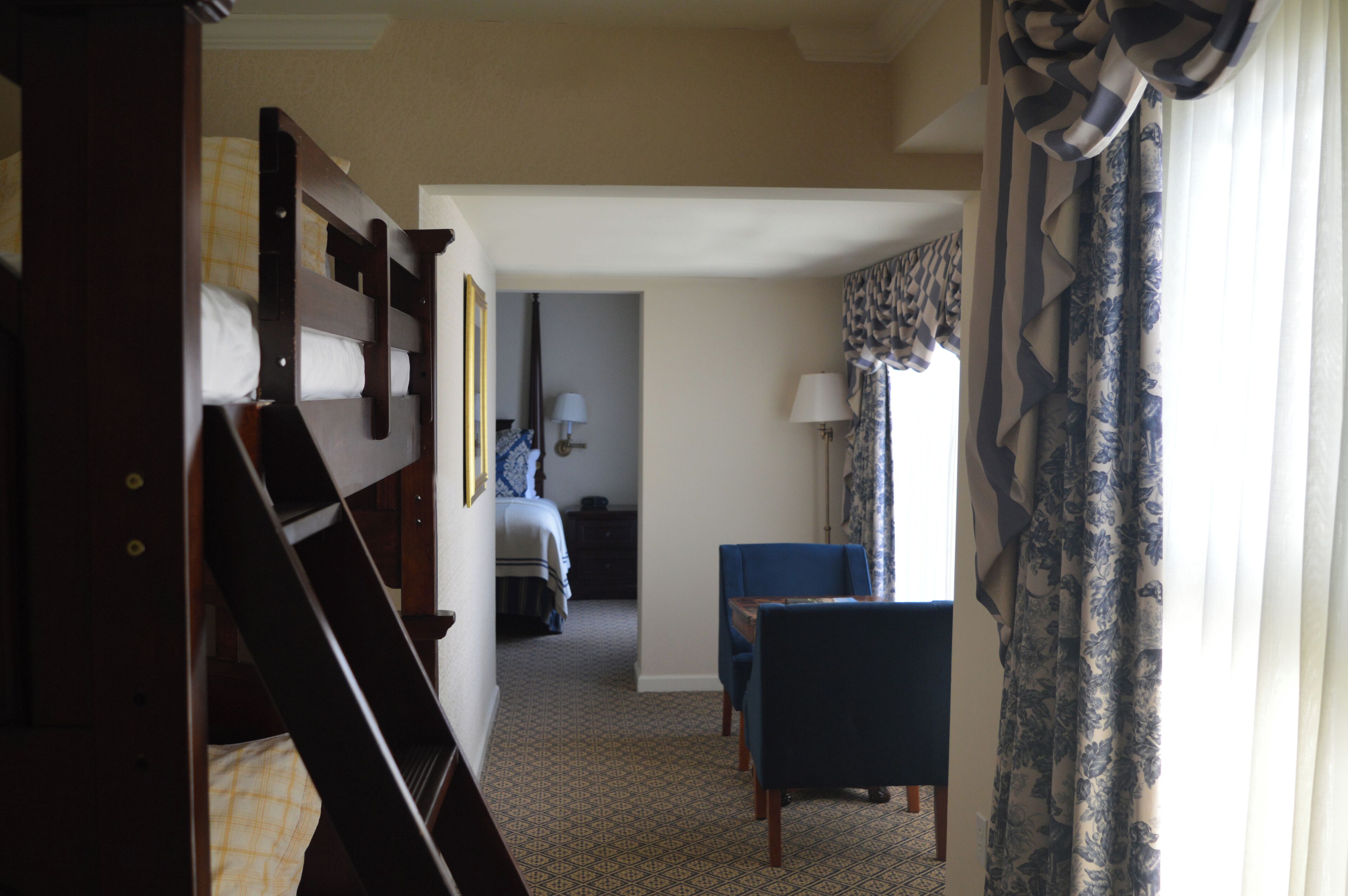 A hotel room with a bunk bed, a desk with a chair, a lamp, and a window with curtains.
