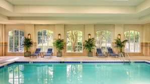 Une piscine intérieure à l’eau d’un bleu limpide, entourée de chaises longues et de plantes en pot.