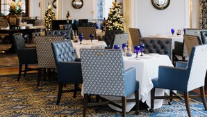 Un espace repas agrémenté d’un lustre, de tables, de chaises et d’un sapin de Noël.