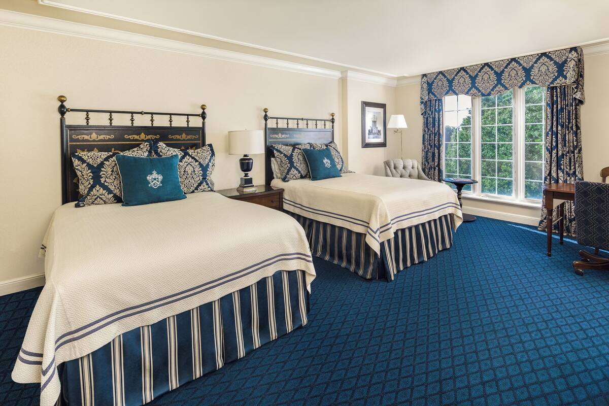 A hotel room with two beds, a large window with curtains, a desk, and a chair.