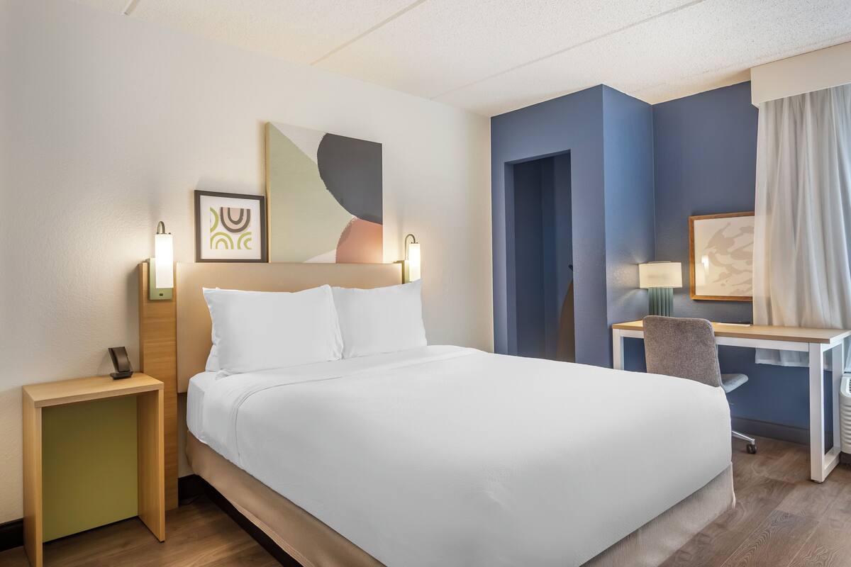 A hotel room with a bed, bedside tables, a desk, and a chair.