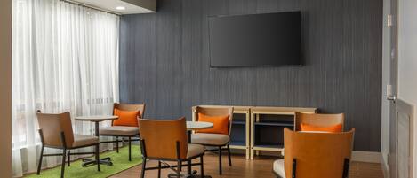 A modern meeting room with a flat-screen TV, wooden tables, and comfortable chairs.