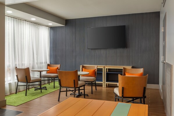 A modern meeting room with a flat-screen TV, wooden tables, and comfortable chairs.