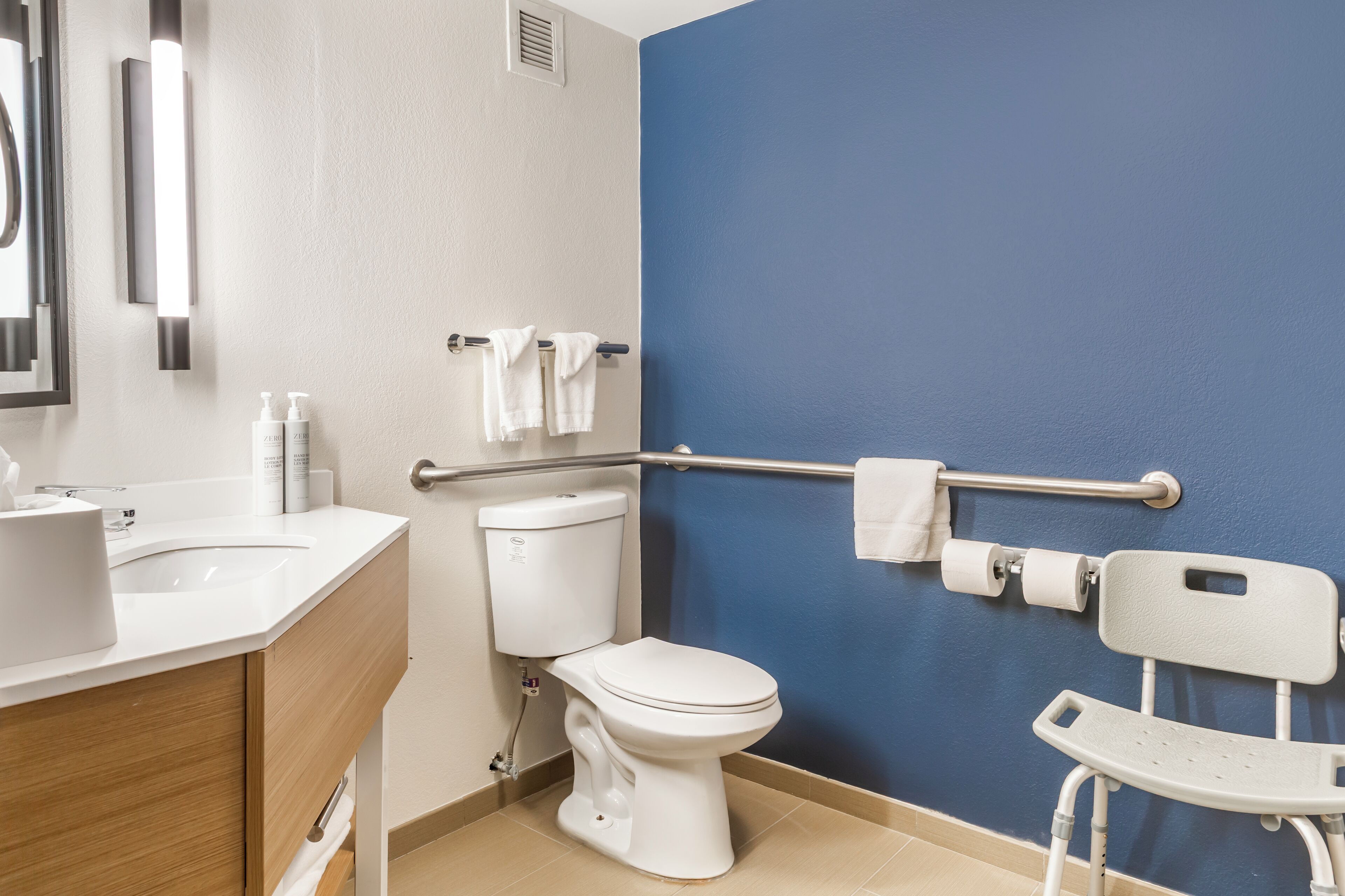 Une salle de bain avec des toilettes blanches, un mur bleu, un lavabo blanc et une barre d’appui blanche.