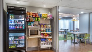 A vending machine area with snacks and beverages, a microwave, and a seating area with tables and chairs. - Spark by Hilton Atlanta Airport South College Park (College Park)