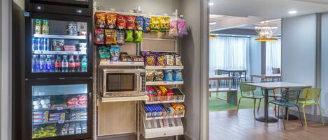 A vending machine area with snacks and beverages, a microwave, and a seating area with tables and chairs.