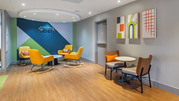 A modern waiting area with a blue and green wall, a circular ceiling light, and three framed artworks. - Spark by Hilton Atlanta Airport South College Park (College Park)