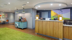 A hotel reception area with a wooden counter, a blue cart, and a green carpet. - Spark by Hilton Atlanta Airport South College Park (College Park)