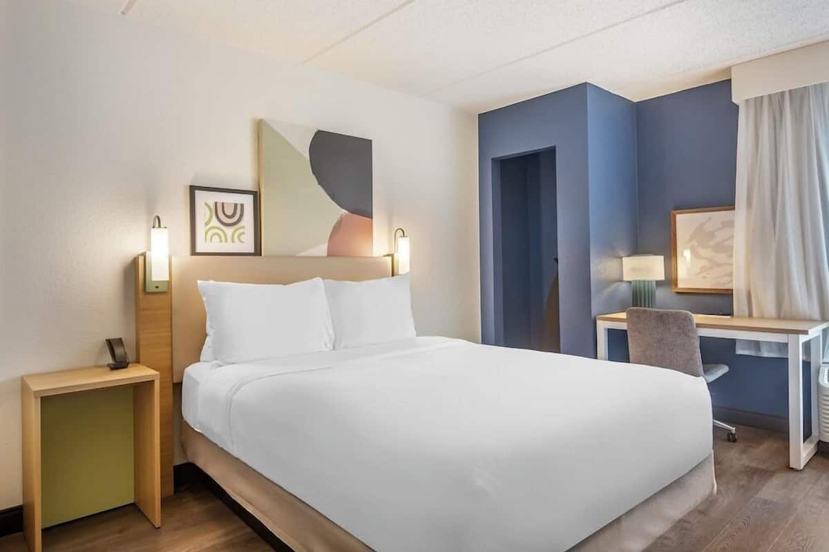 A hotel room with a bed, bedside tables, a desk, and a chair.