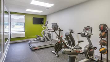A gym with treadmills, an elliptical, and a stationary bike. There are exercise balls on a rack.