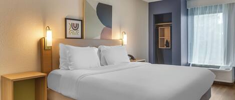 Habitación de hotel con una cama grande, mesitas de noche, una obra de arte colgada en la pared y una ventana con cortinas.
