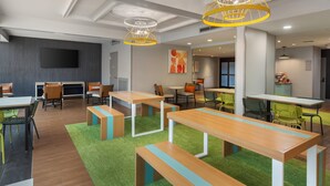 A modern dining area with wooden tables and benches, green chairs, and a flat-screen TV mounted on the wall. - Spark by Hilton Atlanta Airport South College Park (College Park)