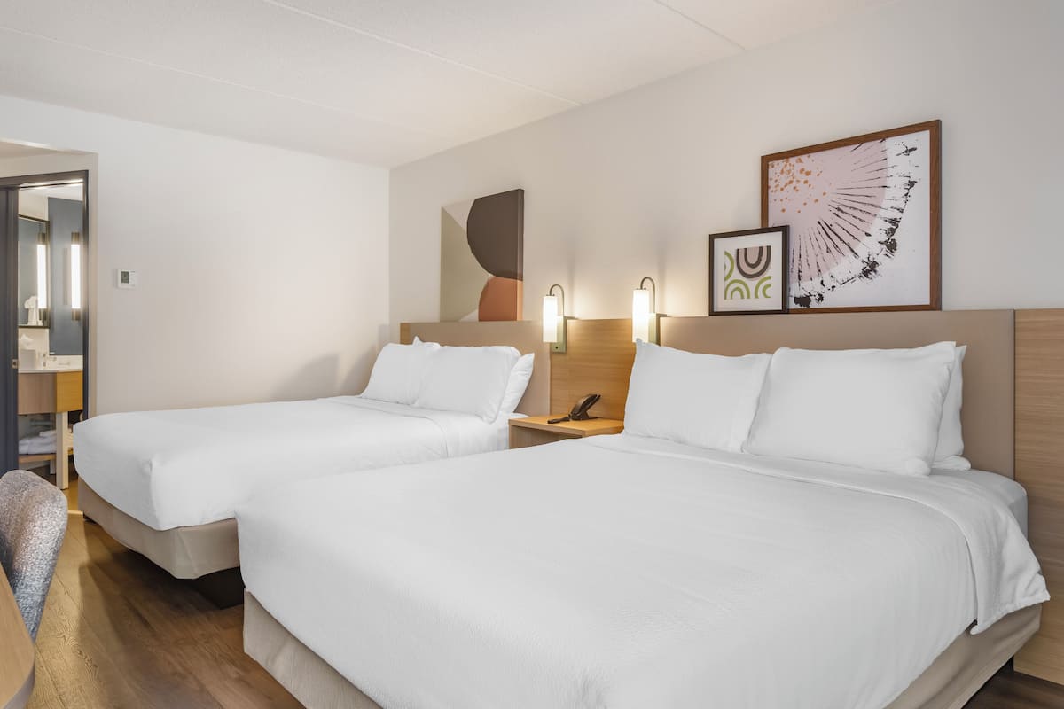A hotel room with two single beds, a wooden headboard, bedside lamps, a phone, and a wall with abstract art.