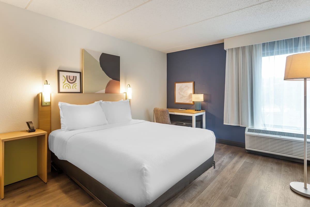 A hotel room with a large bed, bedside tables, a desk, a chair, and a window with curtains.