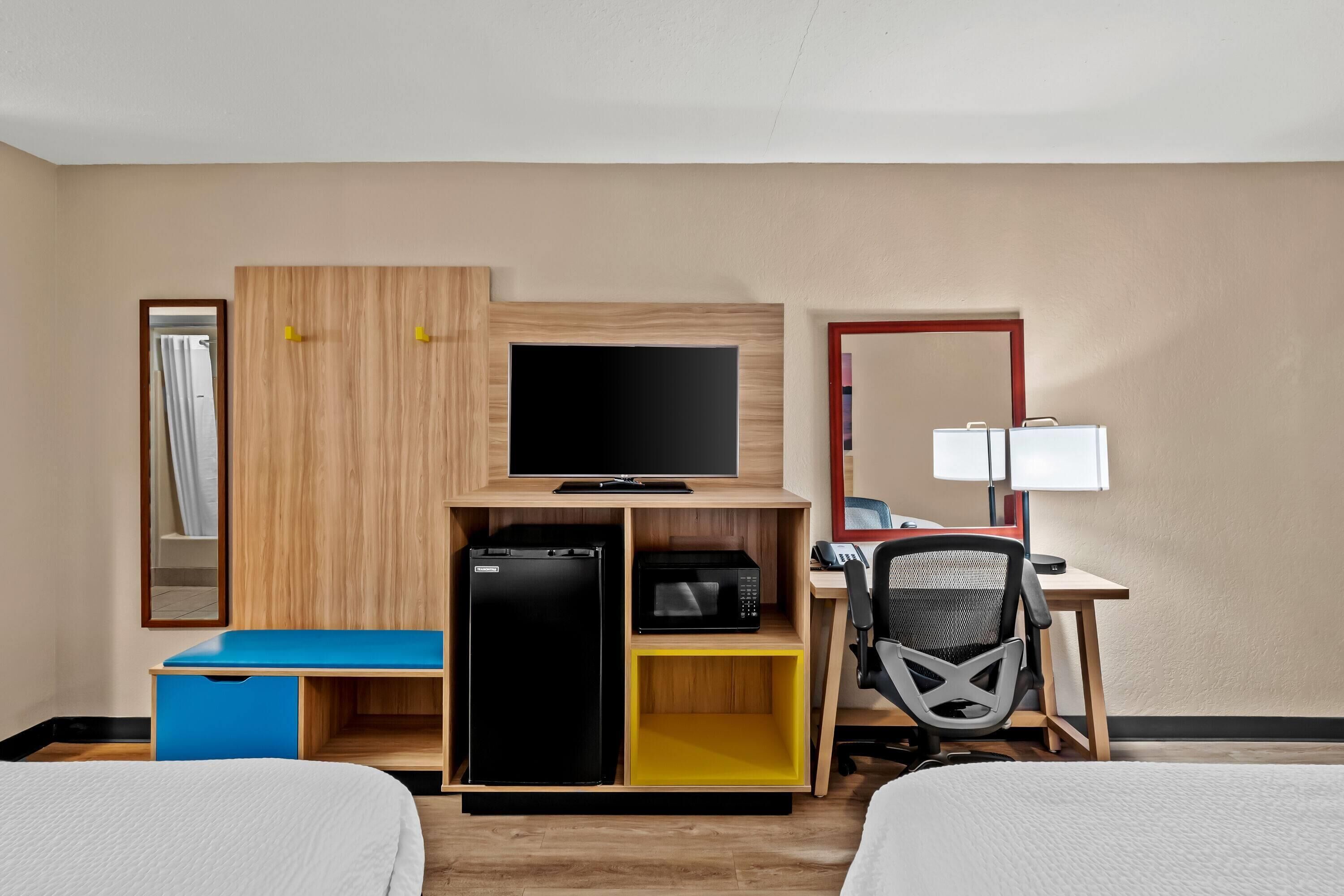 A hotel room with a bed, a desk with a chair, a television, a microwave, and a refrigerator.