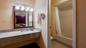 Ein Badezimmer mit Granitwaschtisch, Waschbecken, einem beleuchteten Spiegel, einer Duschkabine mit Vorhang und Toilette.