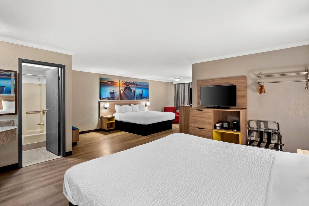 A hotel room with a large bed, a TV, a desk, and a painting of a pier.