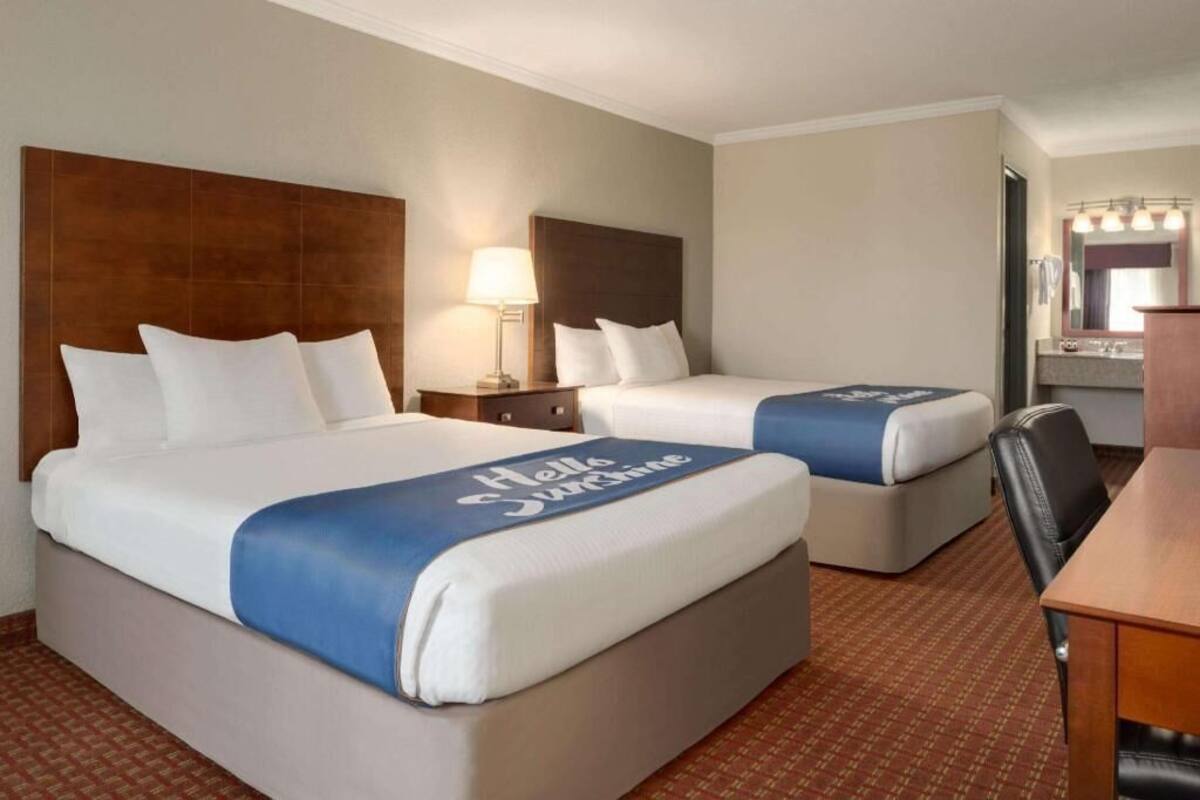 A hotel room with two beds, a desk, and a mirror.