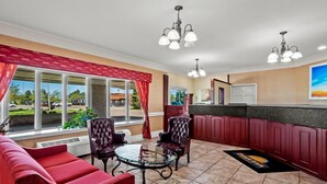 Eine Hotelhalle mit einem roten Sofa, zwei Sesseln, einem Glastisch und einer Küchenzeile mit roten Schränken und einer Arbeitsplatte.