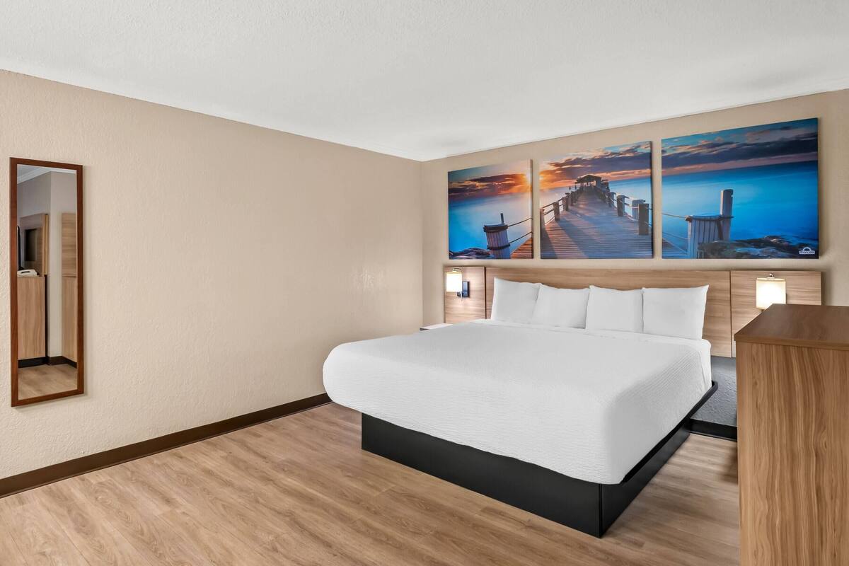 A hotel room with a large bed, a wooden headboard, a nightstand, and a wall-mounted mirror.