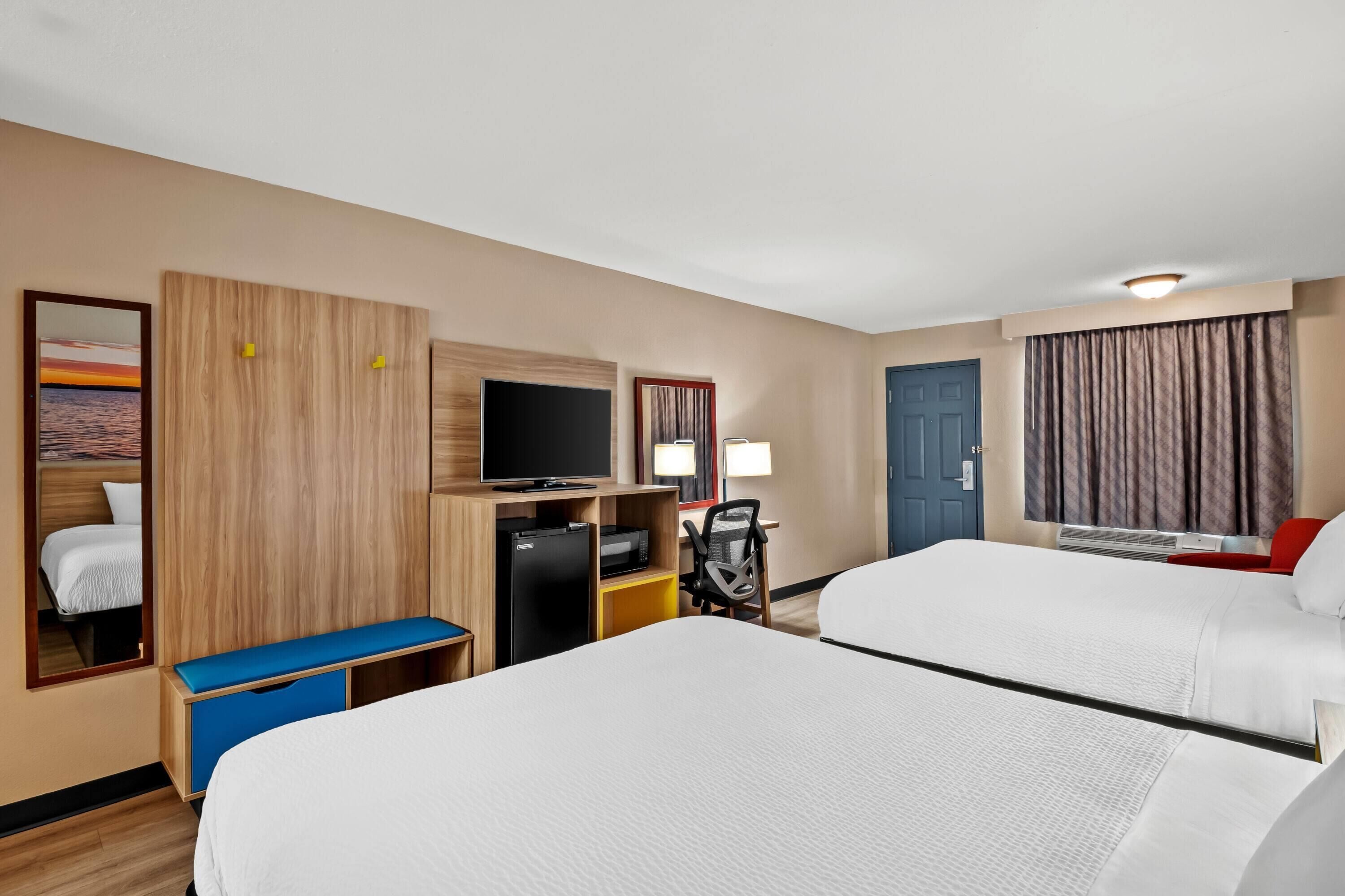 A hotel room with two beds, a desk with a computer, a TV, and a window with curtains.