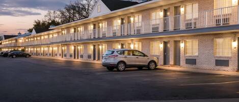 Un motel con varias habitaciones, una zona de estacionamiento techada y un coche estacionado al frente.
