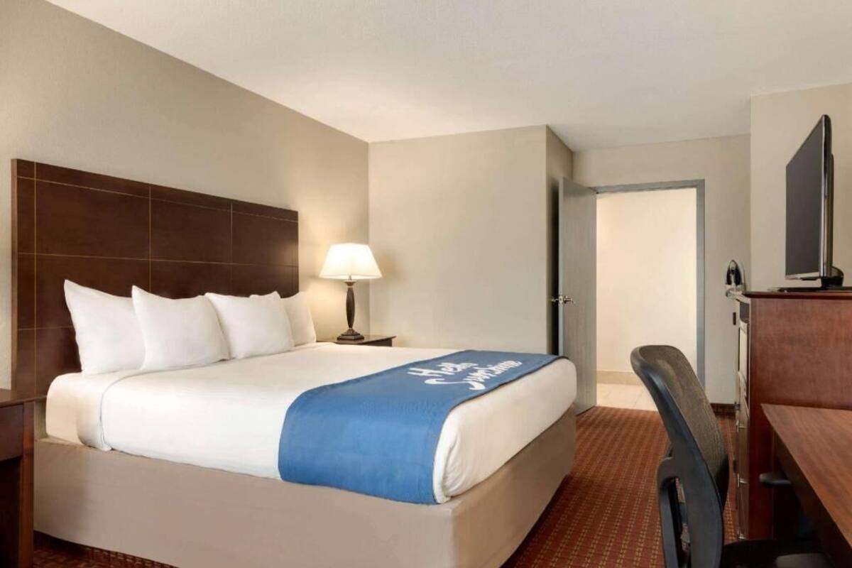 A hotel room with a bed, a desk, a chair, a lamp, and a television.