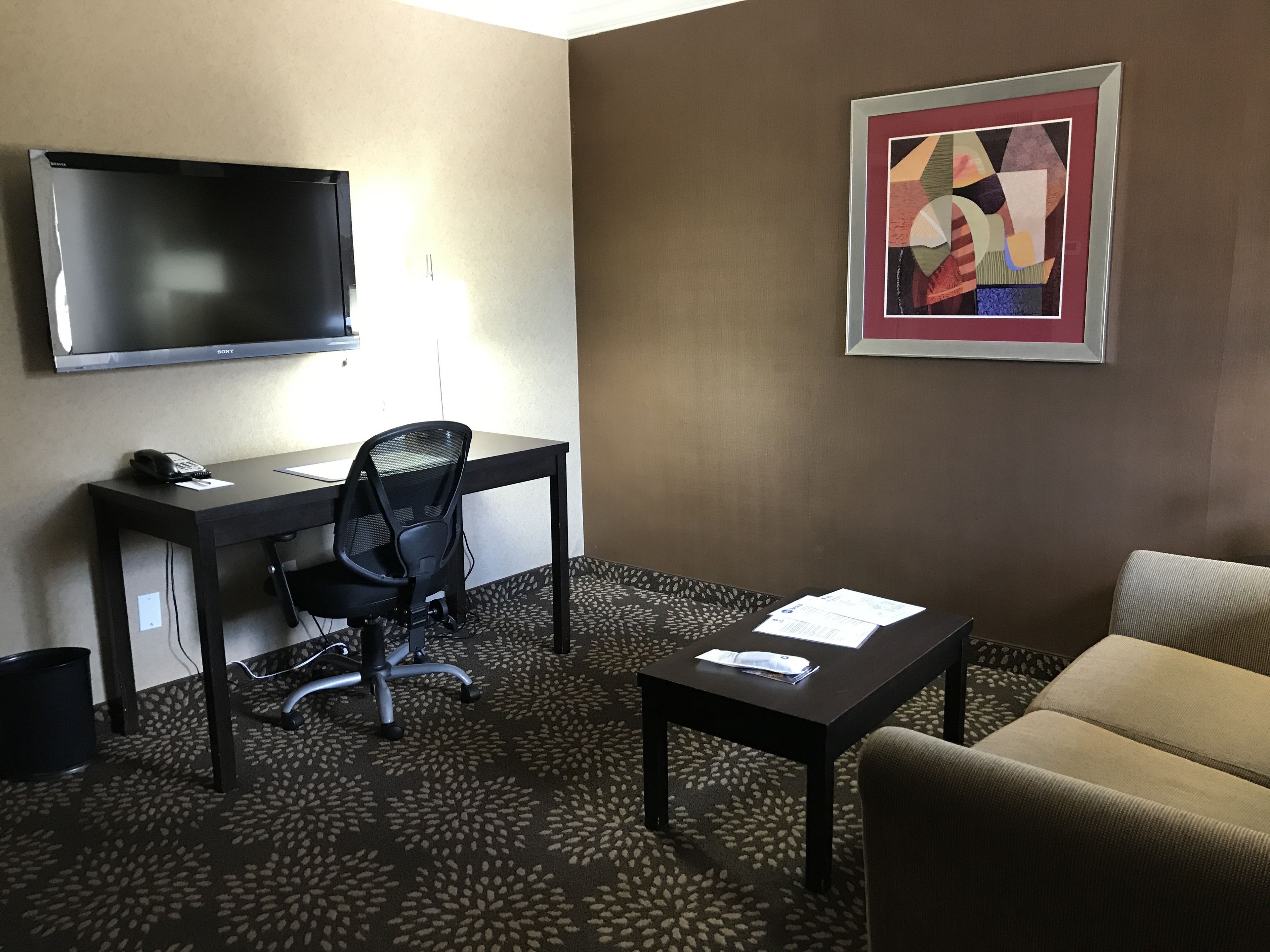 Une chambre d’hôtel équipée d’un bureau, d’une chaise, d’une télévision, d’un canapé et d’un tableau abstrait encadré.