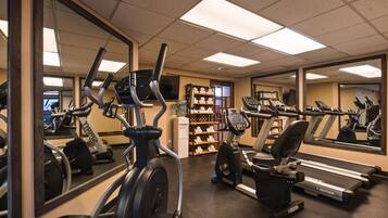 A gym with various cardio machines, a water dispenser, and a mirror reflecting the equipment.