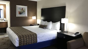 Een hotelkamer met een groot bed, een nachtkastje met een lamp, een stoel en een ingelijst schilderij aan de muur.