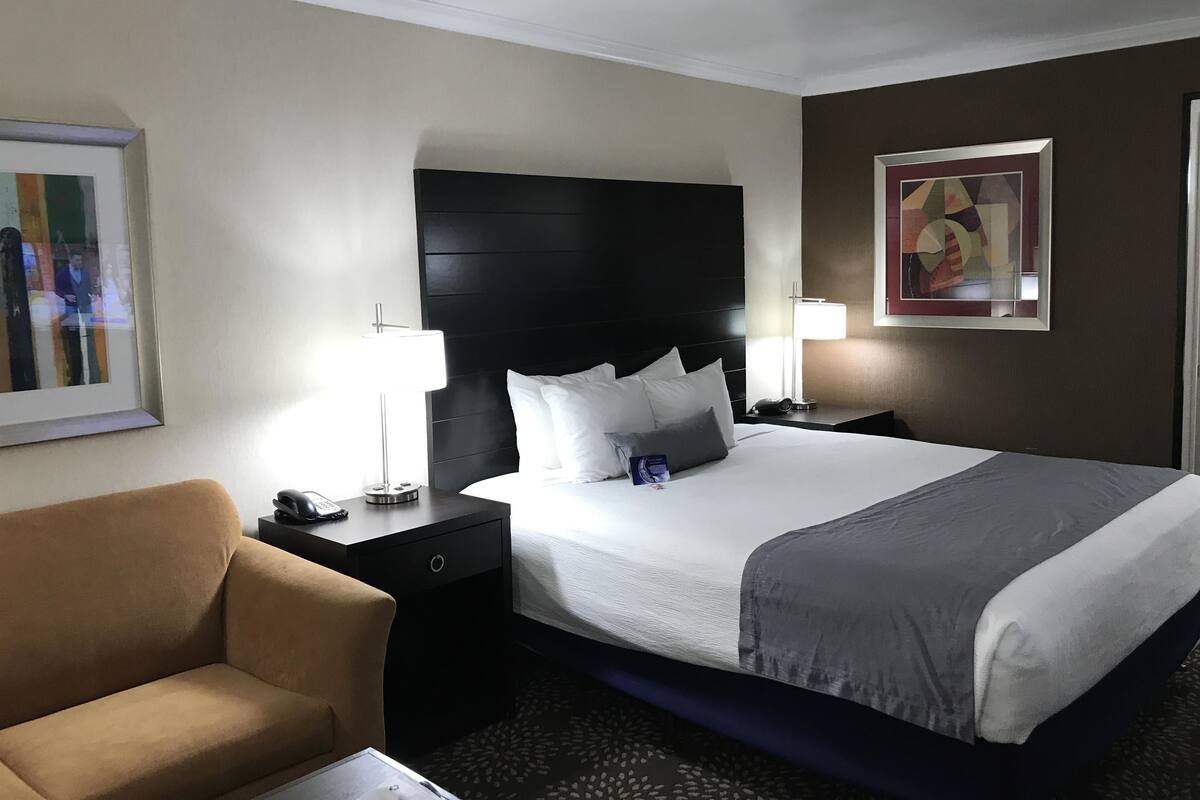 A hotel room with a large bed, a bedside table with a lamp, a chair, and artwork on the walls.