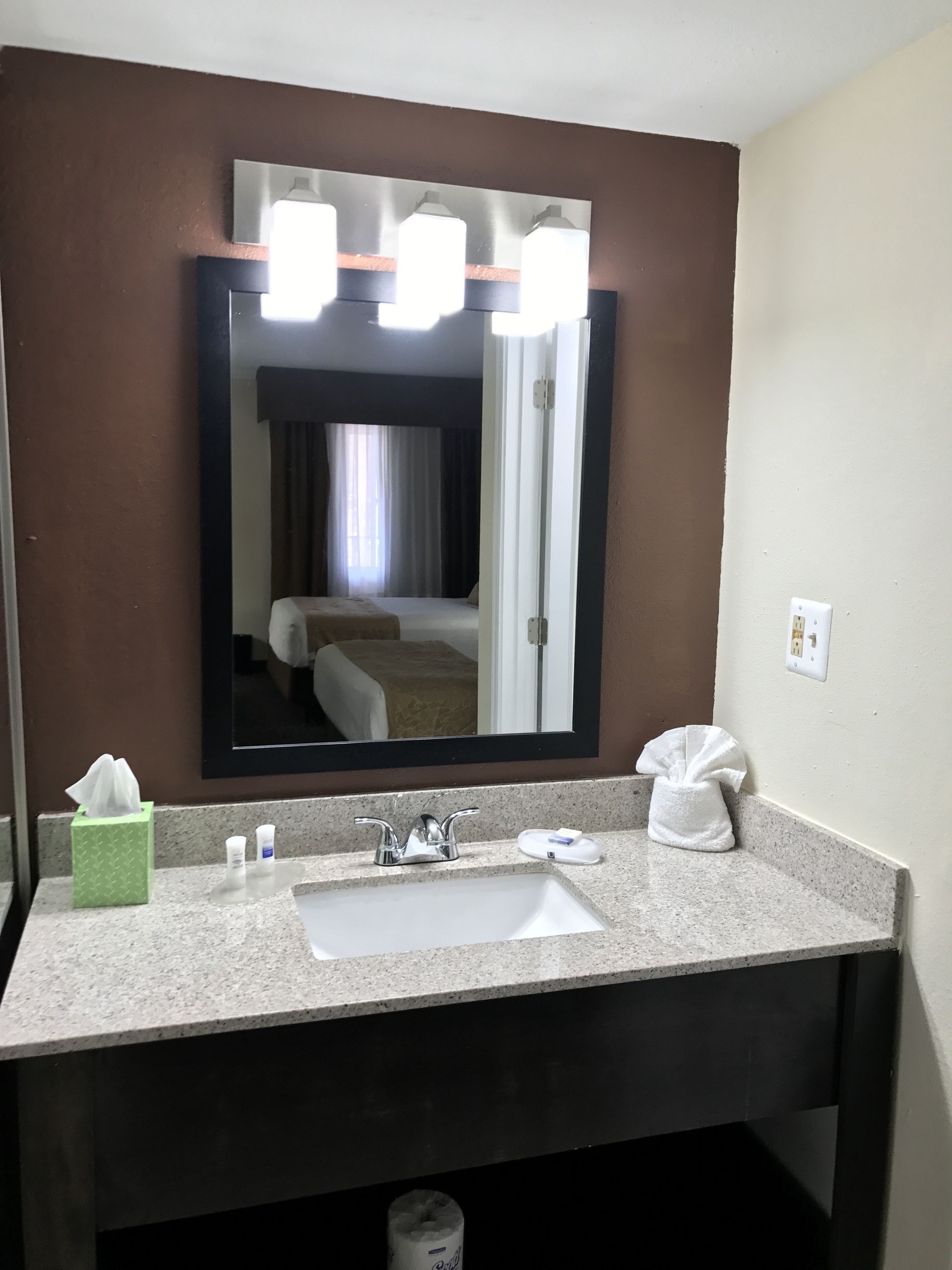 A hotel bathroom with a large mirror, a sink with toiletries, and a towel dispenser.
