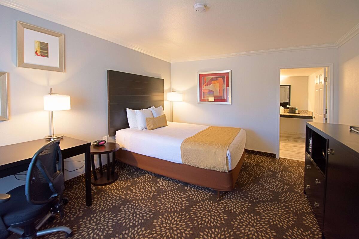 A hotel room with a bed, desk, chair, lamp, and artwork on the walls.