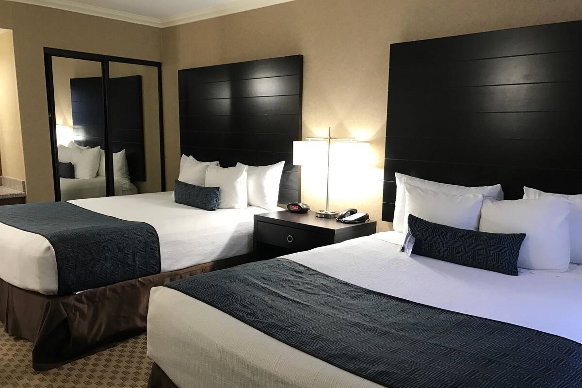 A hotel room with two beds, a nightstand, a lamp, and a mirror.