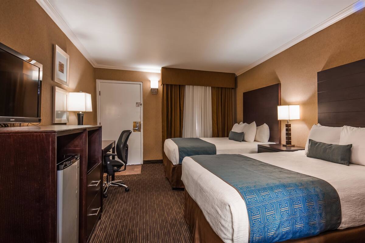 A hotel room with two beds, a desk with a chair, a TV, and a door.