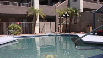 A swimming pool with a sun design, surrounded by palm trees and a multi-story building with balconies.
