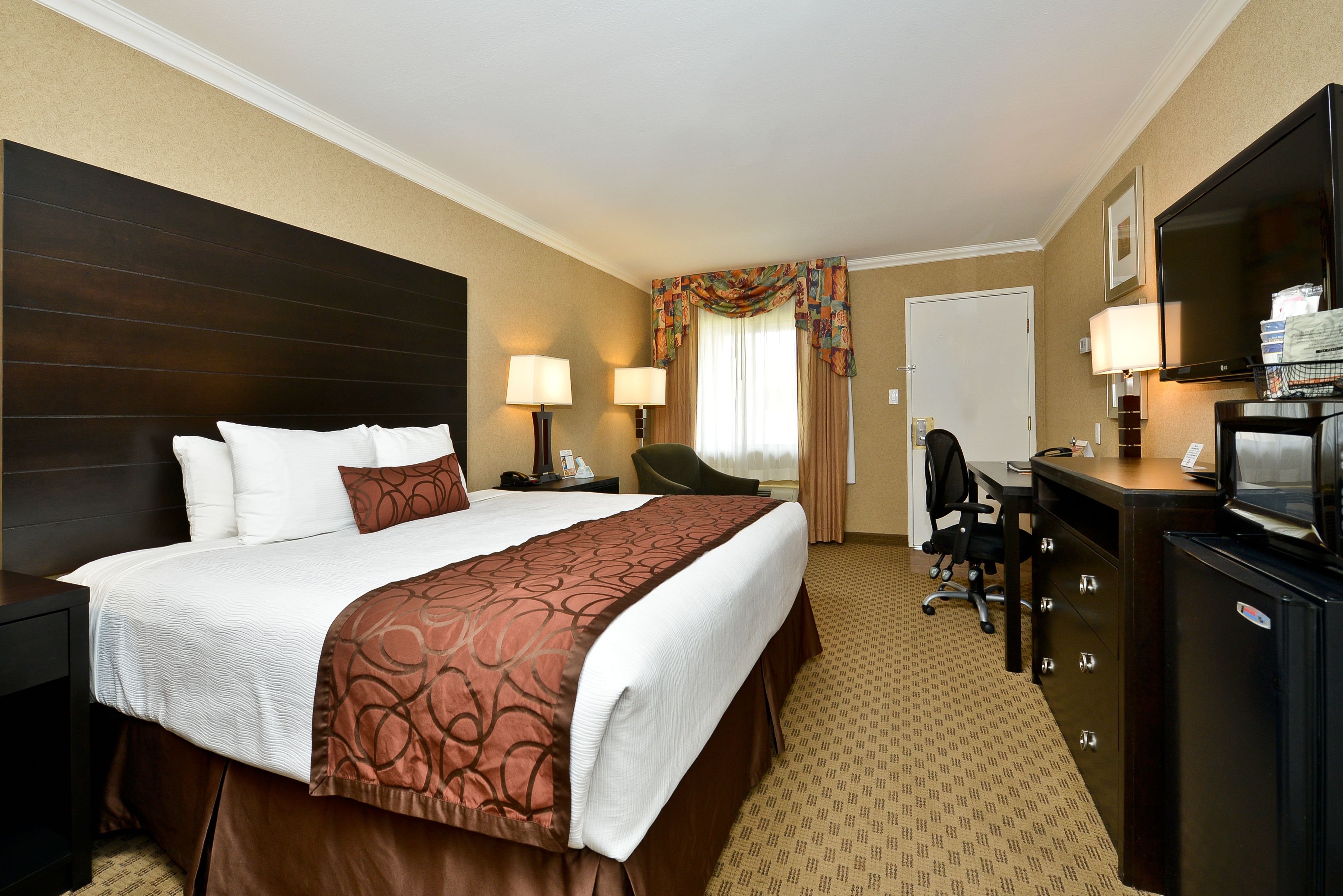 Une chambre d’hôtel avec un grand lit, un bureau, une chaise, une télévision et une armoire.