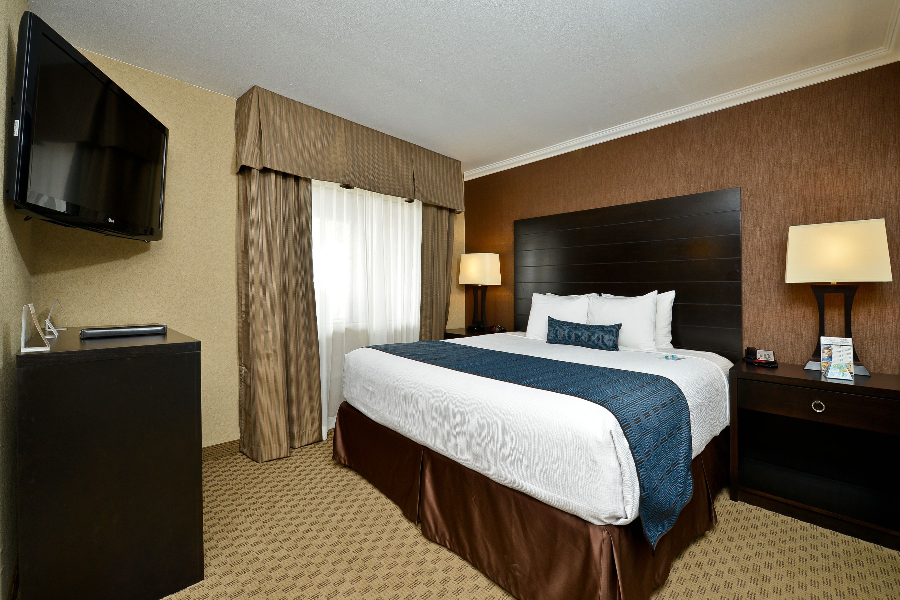 Habitación de hotel con una cama grande, un televisor de pantalla plana en la pared, un escritorio y una mesita de noche con lámpara.