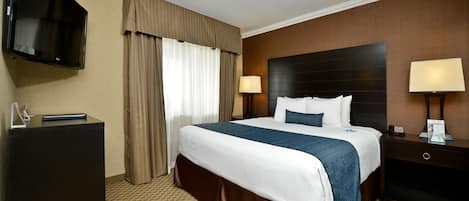Habitación de hotel con una cama grande, un televisor de pantalla plana en la pared, un escritorio y una mesita de noche con lámpara.