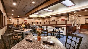 A hotel dining area with multiple tables and chairs, some with floral centerpieces. - Heritage Inn (Great Falls)