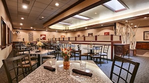 A hotel dining area with multiple tables and chairs, some with floral centerpieces. - Heritage Inn (Great Falls)