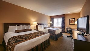A hotel room with two beds, a desk, a television, and a chair. - Heritage Inn (Great Falls)