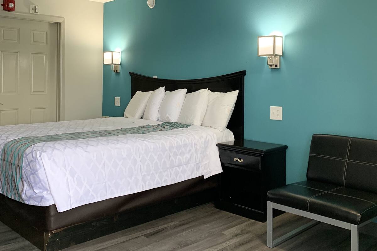 A bedroom with a bed, bedside tables, a bench, and a wall-mounted light fixture.