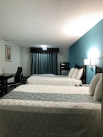 A hotel room with two beds, a desk, a chair, a microwave, and a lamp.