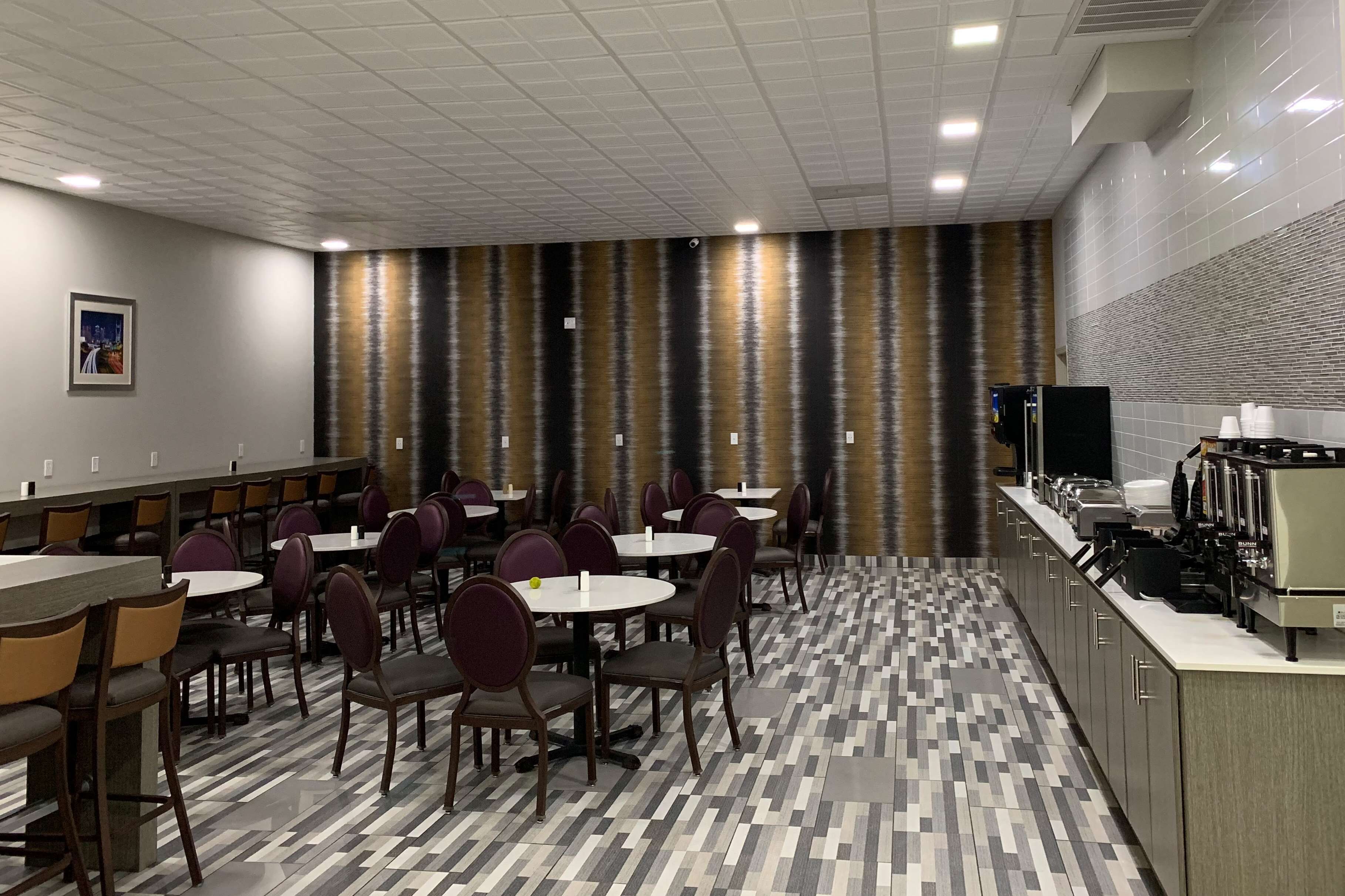 Un comedor de hotel con varias mesas y sillas, una barra de cocina con electrodomésticos y un suelo estampado.